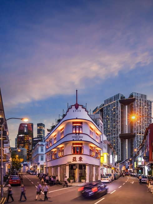 A view of a busy downtown city in singapore at dusk – people are crossing the street and cars are driving by.