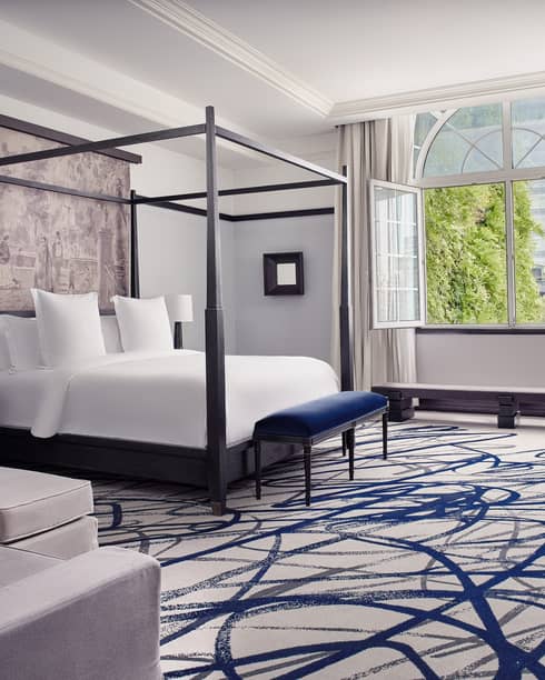 Presidential Suite with four-poster bed, bay window, grey armchair and ottoman, blue patterned carpet