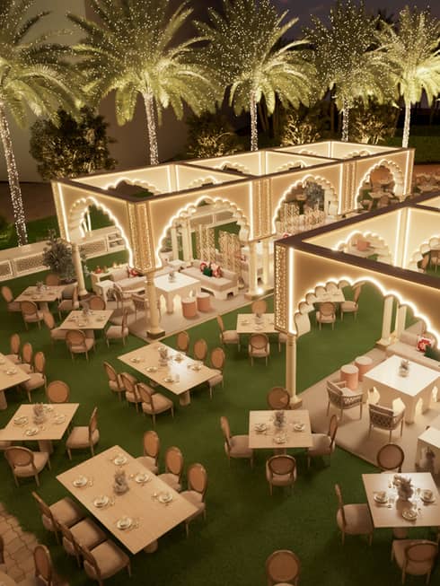Overhead view of outdoor lawn filled with various size tables with some set up beneath two rows of Arabian-style archways edged with lights, all surrounded by palm trees beneath an evening sky