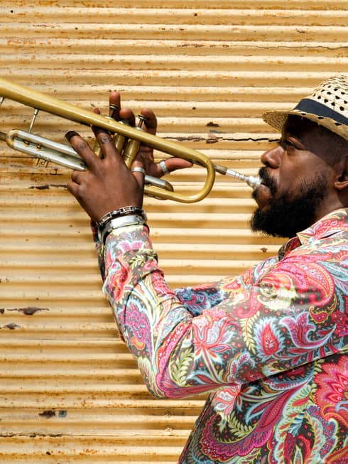 A man in a hat and colourful shirt playing a trumpet.