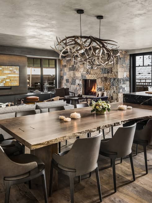 Mountain-chic dining area with wooden floors, dining table and ten leather chairs, antler chandelier
