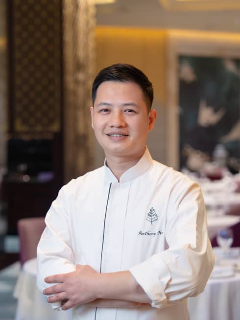Smiling Asian man with arms crossed in white chef's jacket with Four Seasons logo