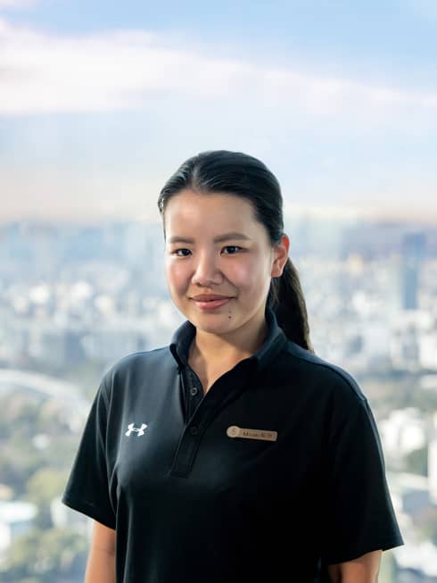 A smiling Resident Senior Fitness Trainer Misaki Kikuchi in a black Under Armour polo shirt and name tag