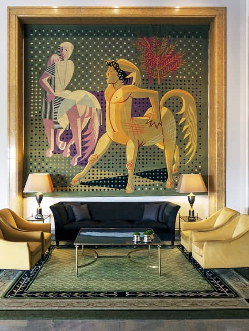 Almada Negreiros Lounge yellow armchairs below large handmade tapestry depicting centaurs