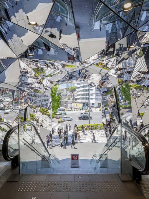 Escalators leading to a mirrored entrance reflecting pedestrians and a busy street scene