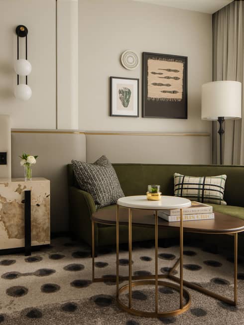 Hotel room lounge area with a green sofa, decorative cushions, modern artwork, adjacent bed and large windows
