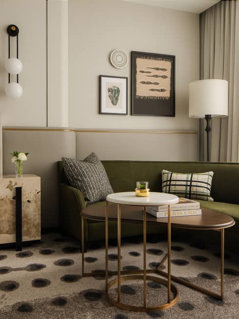 Hotel room lounge area with a green sofa, decorative cushions, modern artwork, adjacent bed and large windows