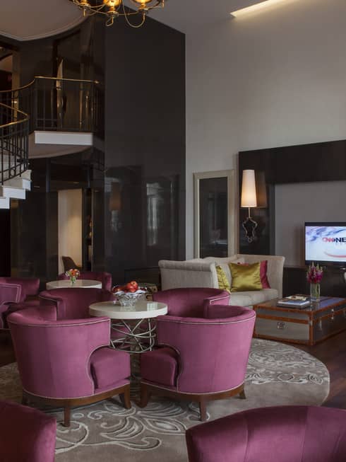 E-Lounge large curved velvet pink chairs around small round tables, modern white spiral staircase in background