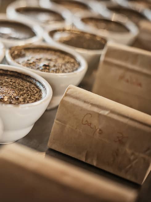Dark coffee in white porcelain ramekins next to kraft paper bags.