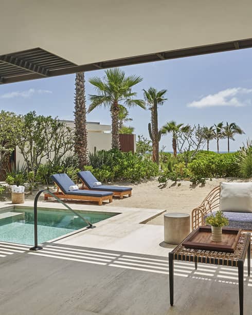 An outdoor area with sofa, chair, lounge chairs and plunge pool.
