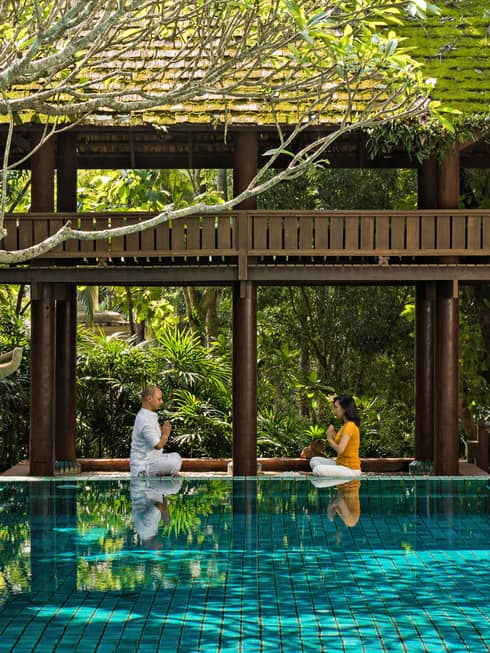 Couple practicing meditation in an outdoor pool setting