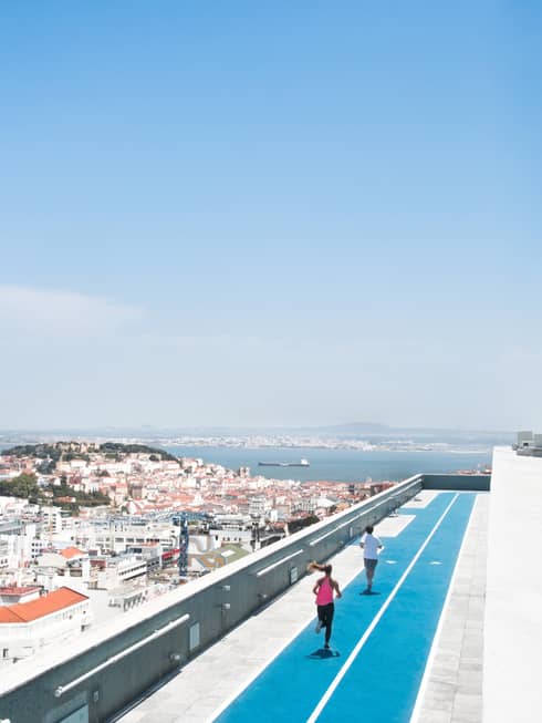 Aerial view of backs of man and woman running on blue rooftop outdoor track, Lisbon city roofs below