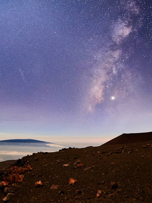 Sunrise under starry sky above mountain, volcanic rocks
