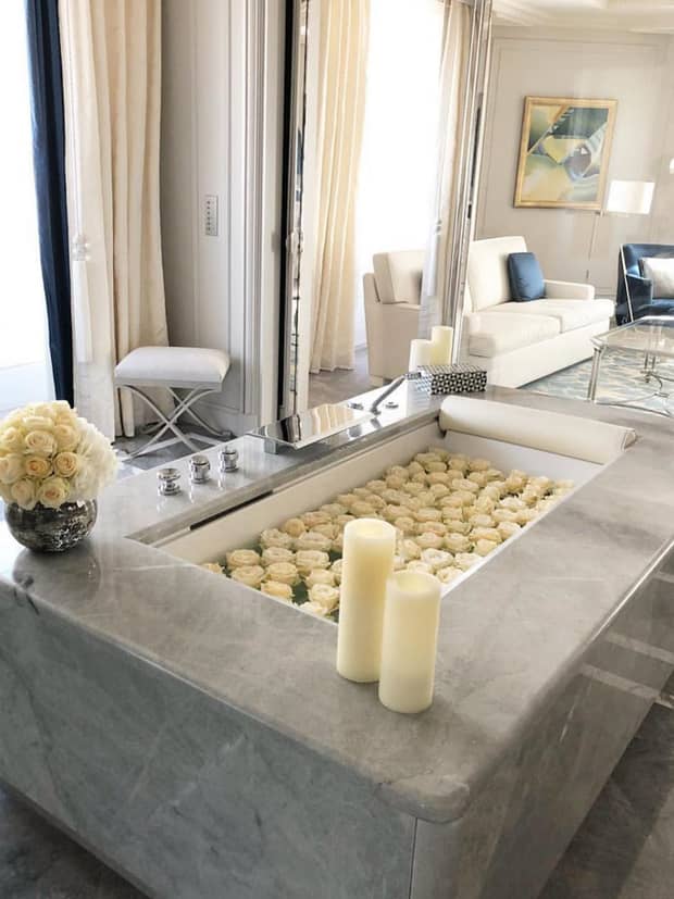 White candles, flowers on grey marble spa tub filled with white roses