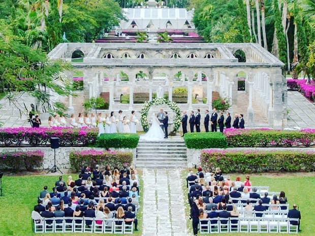 wide shot of wedding ceremony outside in the jungle, with guests and a white architecture behind the bride and groom