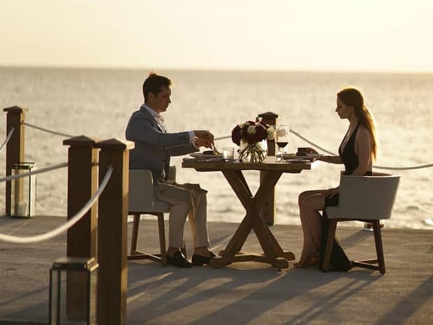 Couple dine at patio restaurant table by water at sunset