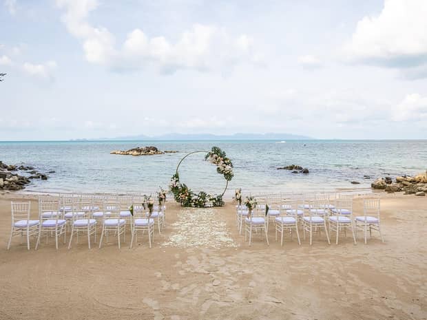 Wedding ceremony, round wedding altar with flowers in front of rows of white chairs on beach