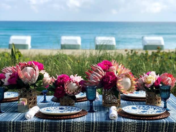 Close-up of outdoor dining table set with elegant plates, tropical pink flowers, ocean in background