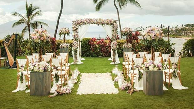 Tropical outdoor wedding ceremony with rows of chairs, flowers and aisle leading to altar under palm trees