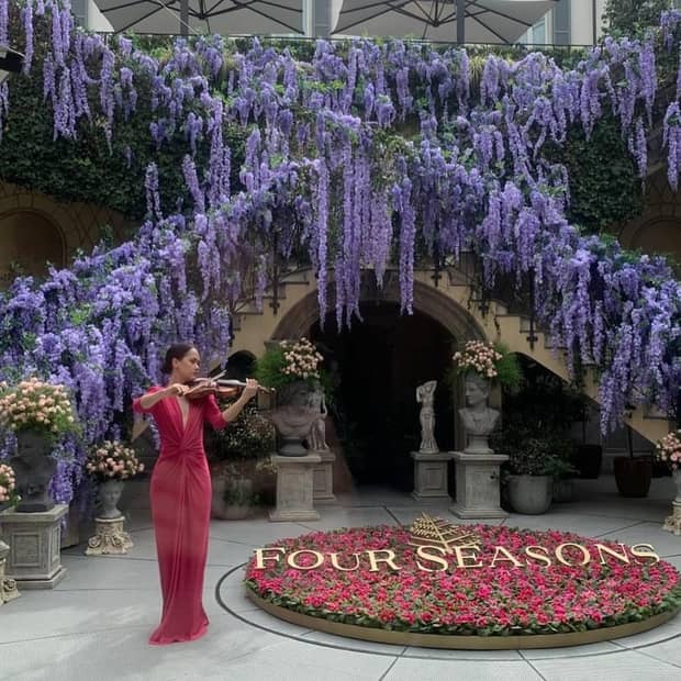 Purple florals engulf an outdoor staircase at Four Seasons Hotel Milano, as a woman in a red gown plays violin beneath