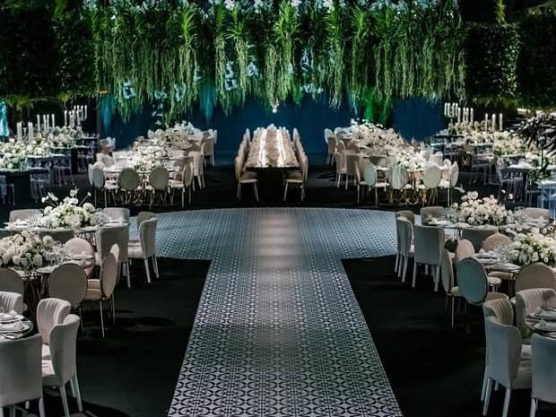Banquet room with decorative aisle, rows of white dining tables under greenery at night