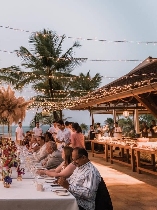Guests enjoy dinner at a tropical outdoor reception under string lights
