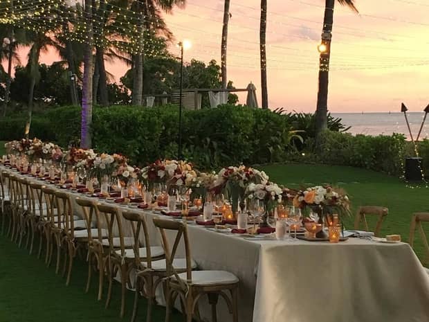 Long banquet wedding dining table with flowers, candles on lawn overlooking ocean