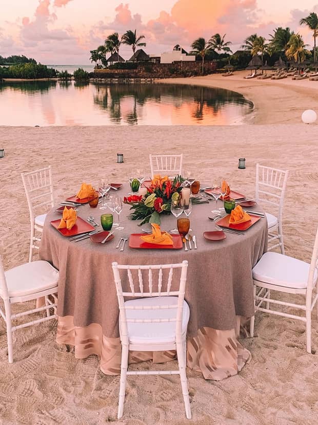Small round wedding dining table with six white chairs on sand beach at sunset