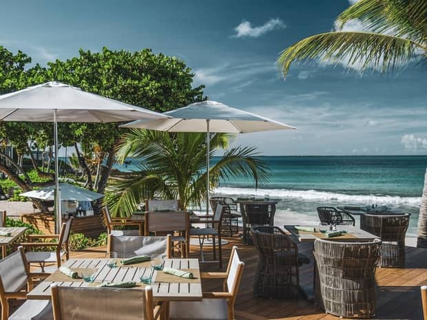 Outdoor beachfront dining area with umbrella-shaded tables overlooking the ocean.