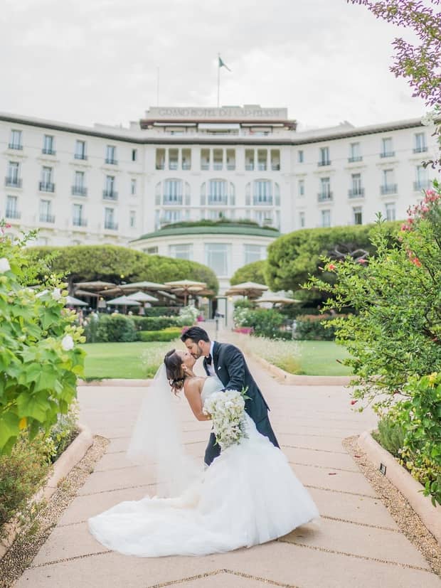 Groom dips bride as they kiss on garden pathway under Four Seasons Hotel exterior