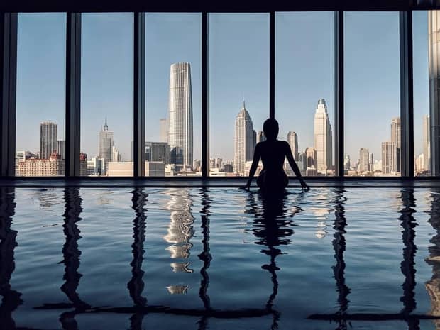 Silhouette of woman sitting on edge of indoor pool by window, city views
