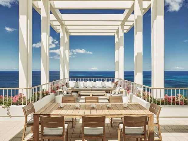 Patio tables, sofas on sunny rooftop patio under pergola, blue sky