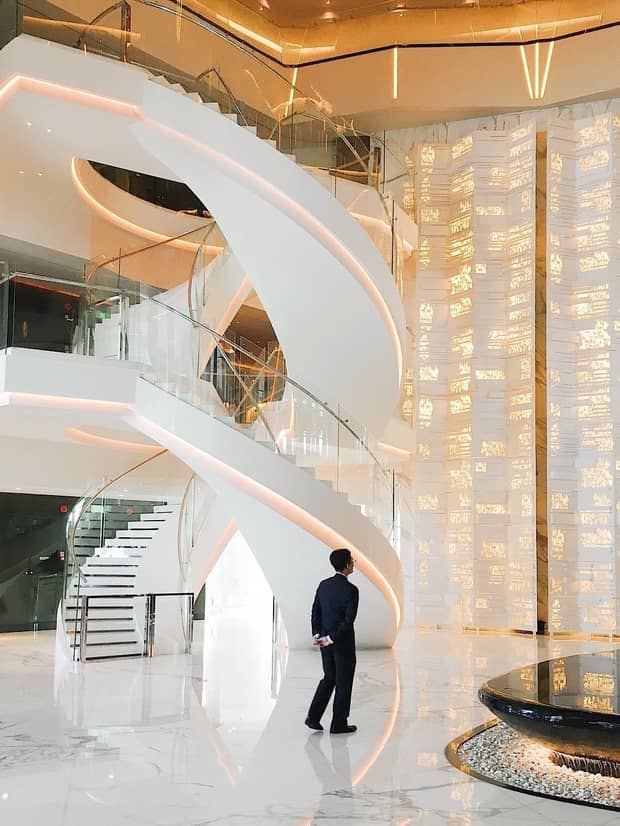 Man wearing suit walks past modern white spiral staircase, wall with gold lights