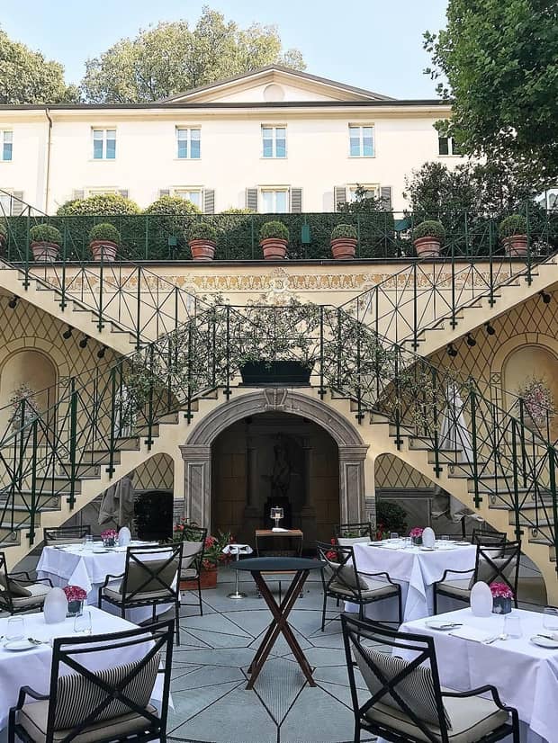 Patio tables with white linens under two connected staircases leading to Four Seasons Hotel Milan