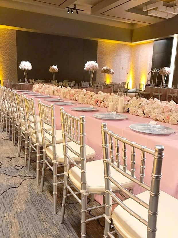 Ballroom with long banquet dining table with pink linens, flowers lined with chairs