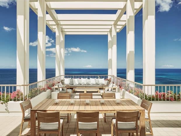 Patio tables, sofas on sunny rooftop patio under pergola, blue sky
