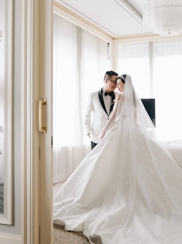 Groom and bride with long wedding dress veil and train pose in hotel suite