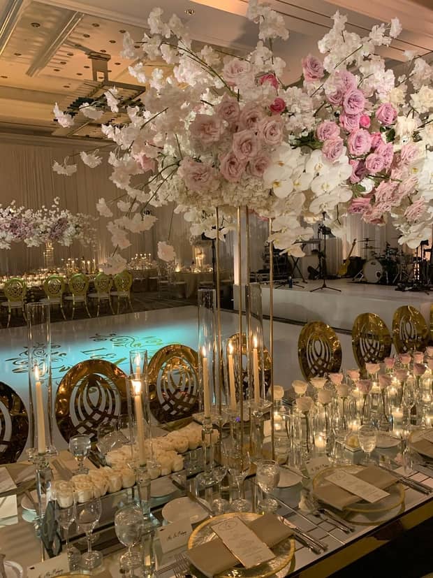 A table with a pink and white flower centerpiece, glasses, and silver plates; a pool can be seen behind the table.