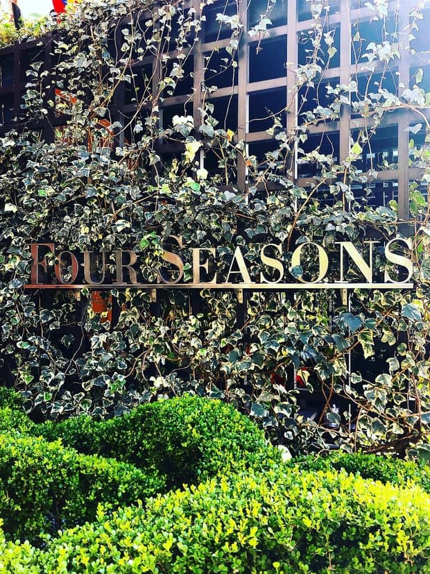 Brass Four Seasons sign against lattice trellis covered in garden vines, greenery