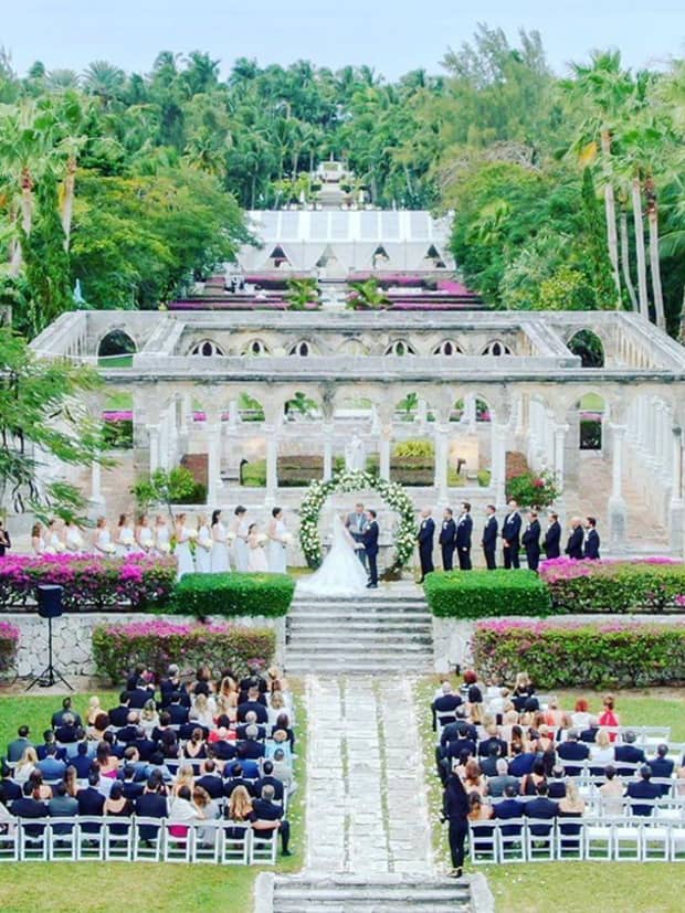 wide shot of wedding ceremony outside in the jungle, with guests and a white architecture behind the bride and groom