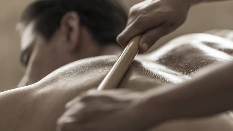 A spa attendant uses a tool to massage a guest's back