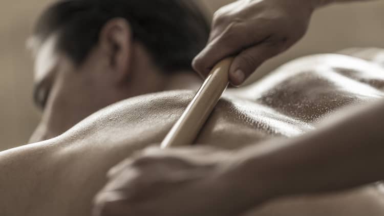A spa attendant uses a tool to massage a guest's back