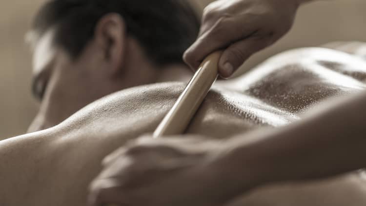 A spa attendant uses a tool to massage a guest's back