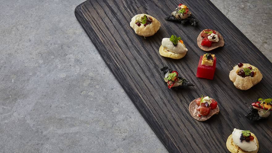 Long dark wood platter with various small gourmet pastries and desserts