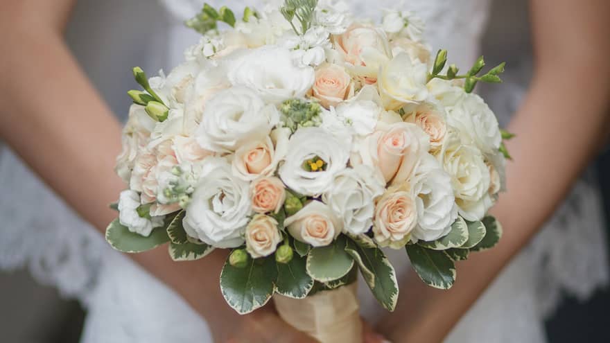 Close up of bride holding wedding bouquet with white and peach roses