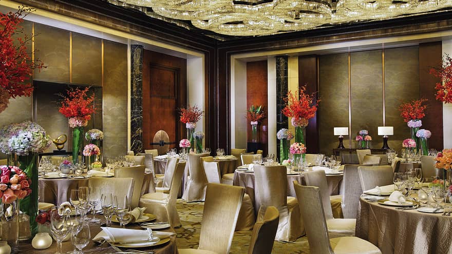 Ballroom banquet tables, red flowers under ceiling with elaborate crystal chandelier design
