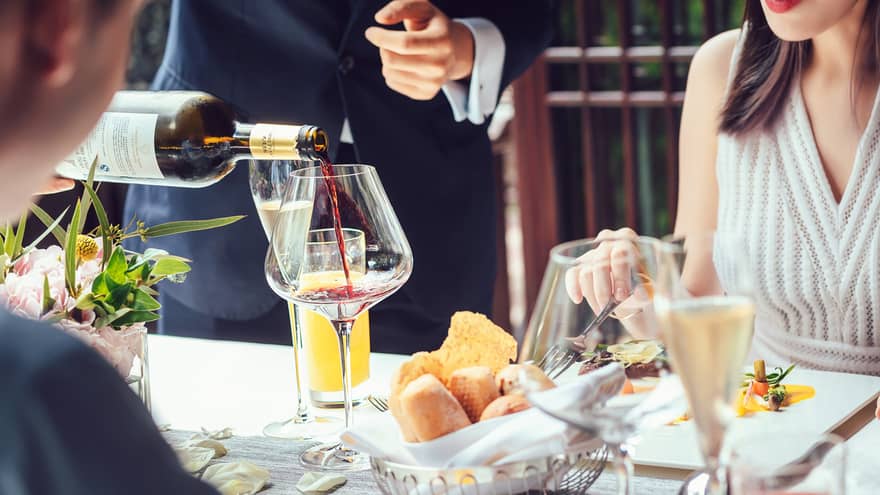 Server pouring red wine into large glass as couple dines at table