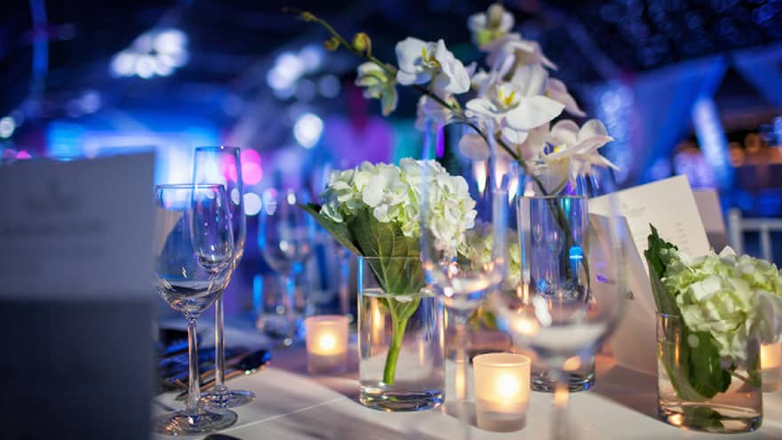 Close up of white flowers, glassware on wedding reception dining table, blue lights in background