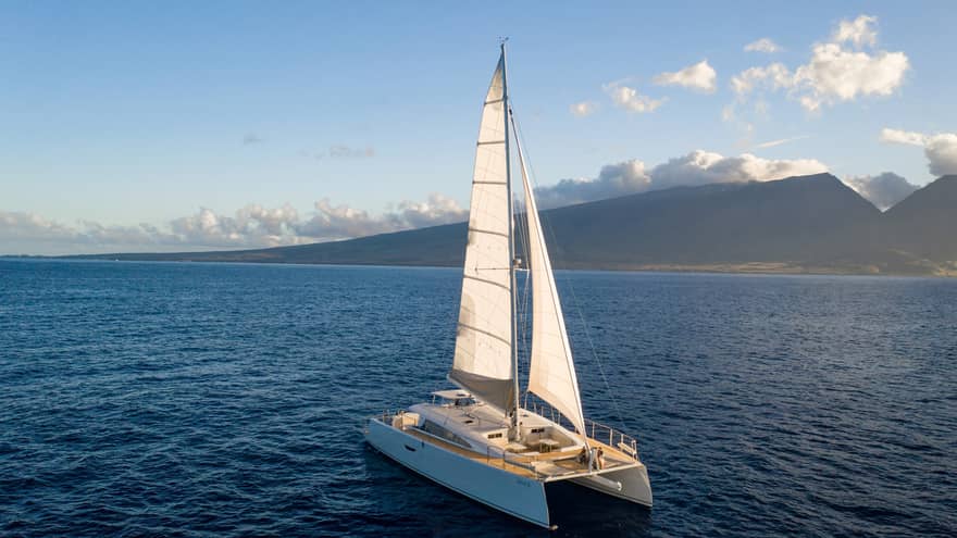Catamaran sailing on the open water against a mountain backdrop