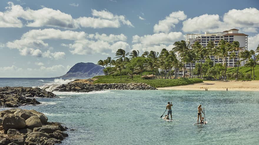 Two people on stand-up paddleboards in lagoon with beach and resort in background